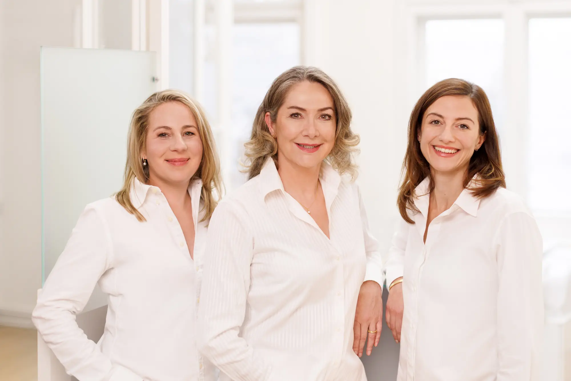 Das Team der Praxis SCHÖNE HAUT in Berlin-Zehlendorf: Dr. med. Meike Schröder mit ihren 2 Kolleginnen, drei Dermatologinnen in weißer Berufskleidung in den hellen Praxisräumen